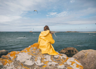 Jeune fille avec un imperméable jaune, assise sur un rocher face à l'océan atlantique