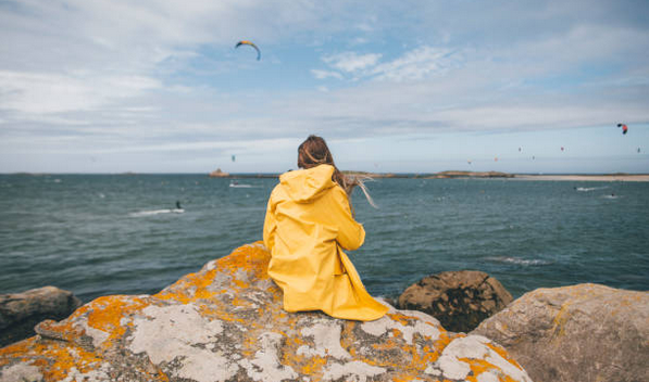 Jeune fille avec un imperméable jaune, assise sur un rocher face à l'océan atlantique